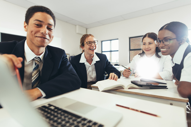 Group of student studying together on a laptop in classroom. Boys and girls in uniform working on a school assignment.